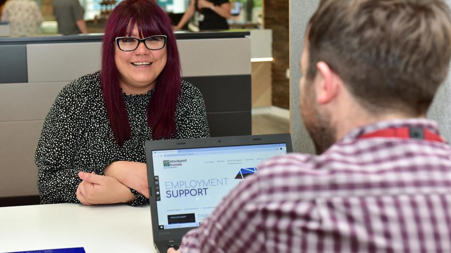 Woman at desk with laptop speaking to man