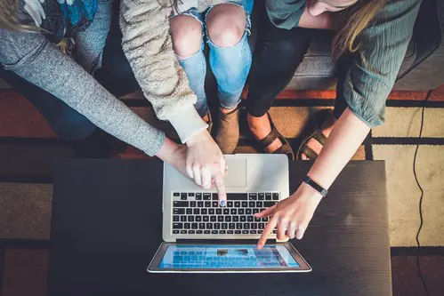 multiple hands pointing to a laptop screen 