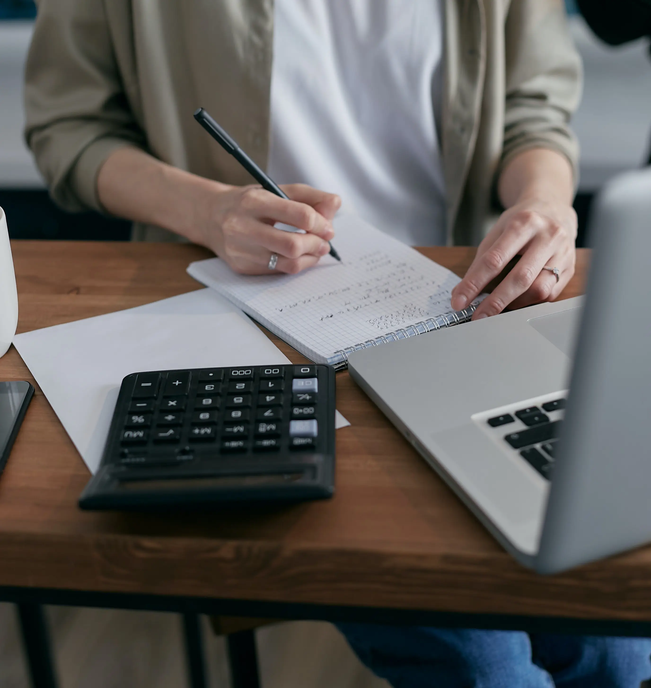 man writing in a notepad with laptop at desk