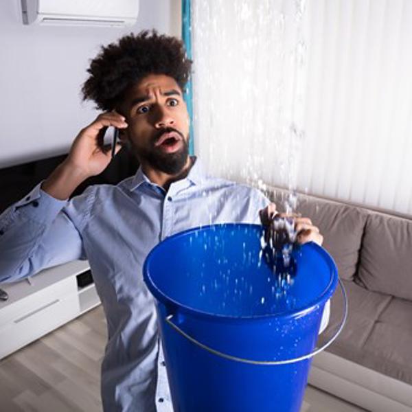 man holding up bucket to leaking ceiling