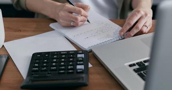 calculator and laptop on desk with hand writing in notepad