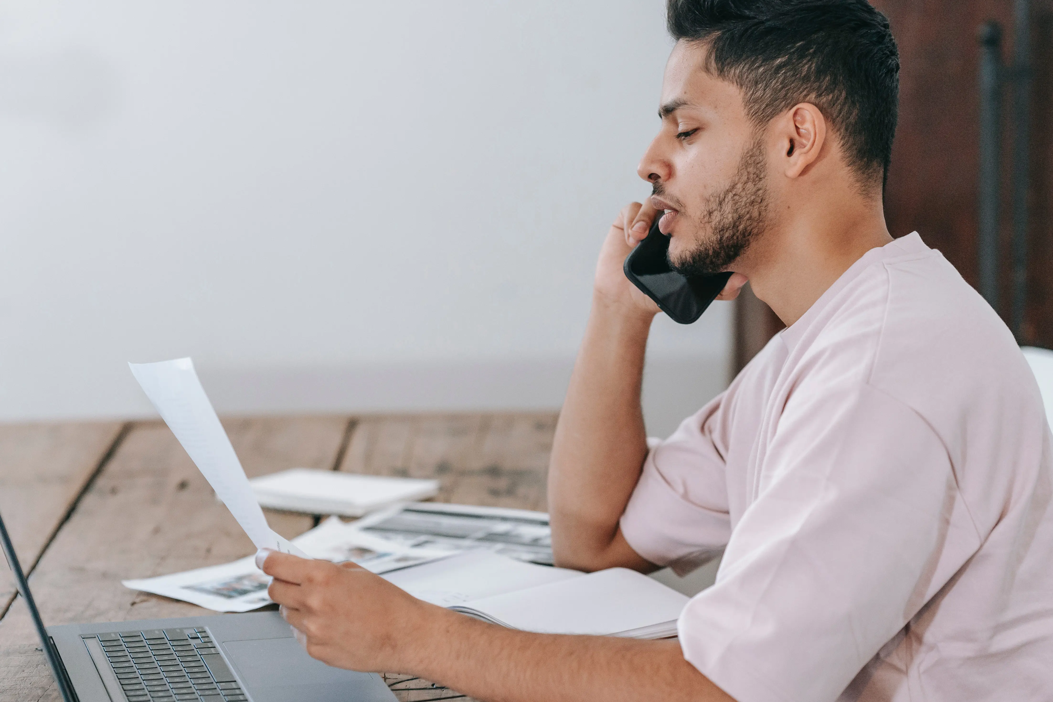 man with phone and paper at laptop