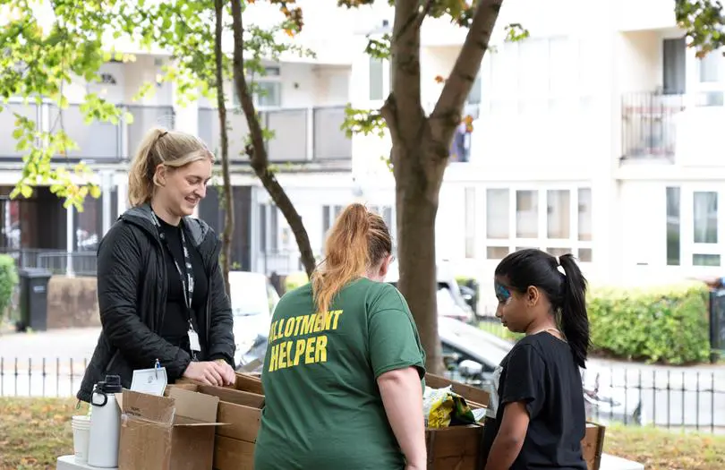 Two woman one wearing a green short helping out a child with boxes