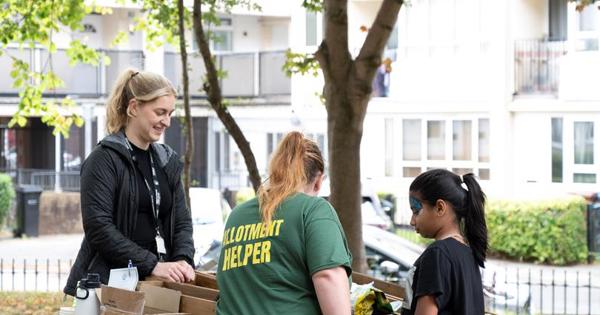 Two woman one wearing a green short helping out a child with boxes