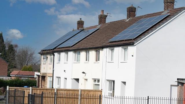 White houses in a row from the side with solar panels seen on their roofs
