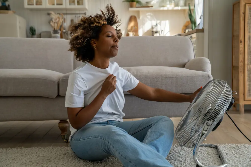 woman inside a housing with fan pointing to her looking warm
