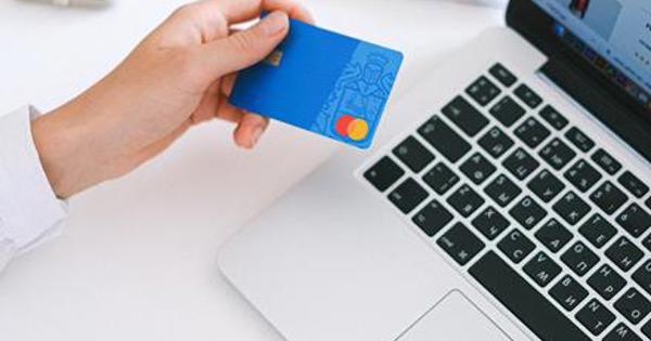 A hand holding a credit card over a laptop