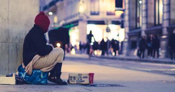 A homeless man on the street looking at people in the distance