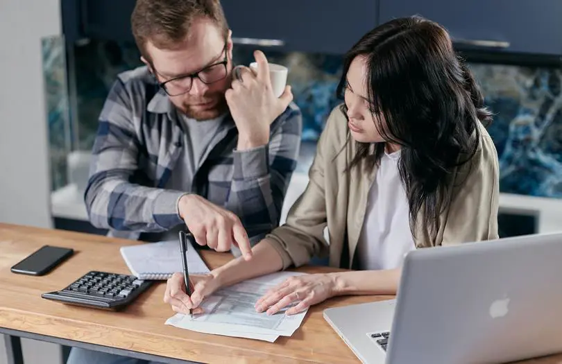 man and woman looking at papers on a desk with a laptop