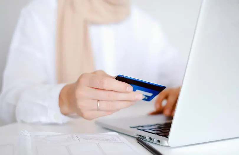 hand holding credit card while typing on laptop
