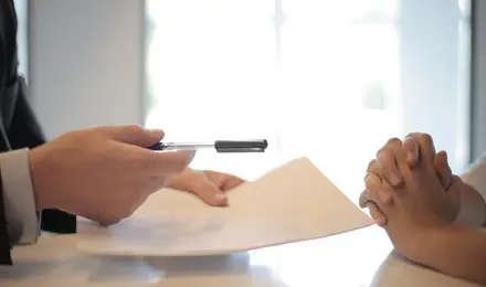 hands holding paper at a desk with other hands together