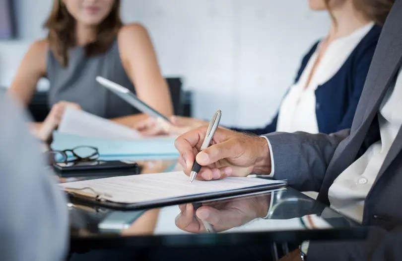 two woman in a board room with paper and pens