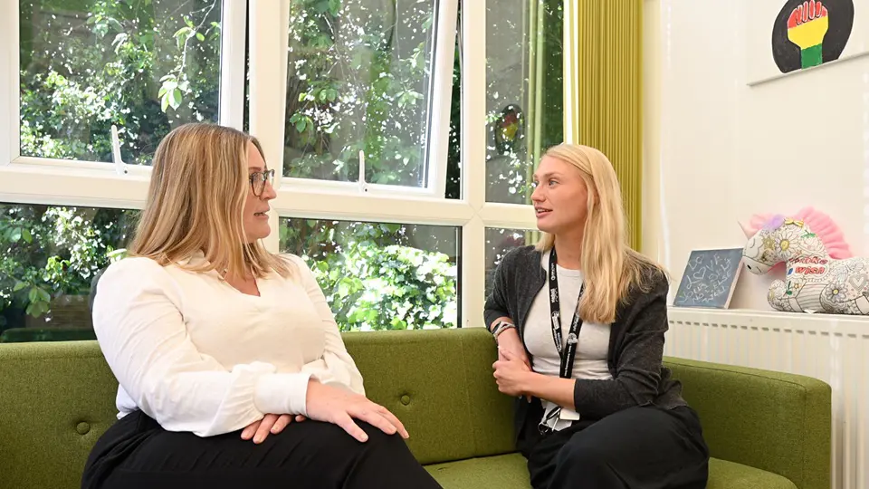 Two Females Talking While Sat On Sofa