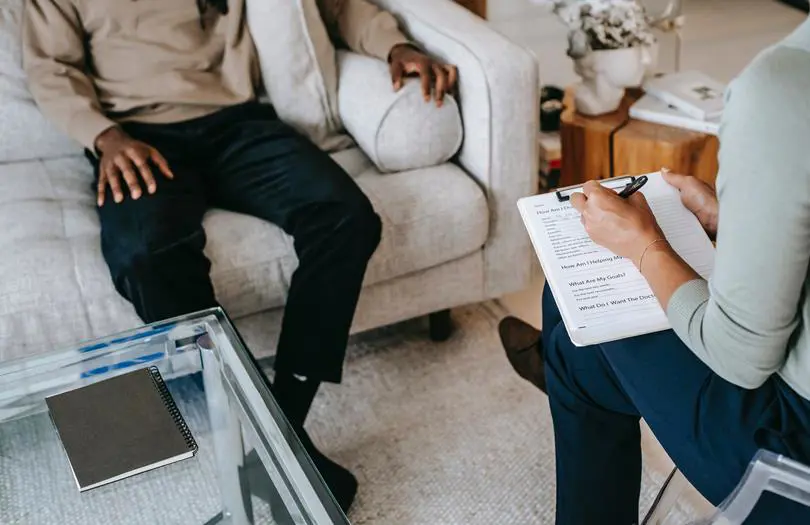 woman writing in notepad with man on sofa