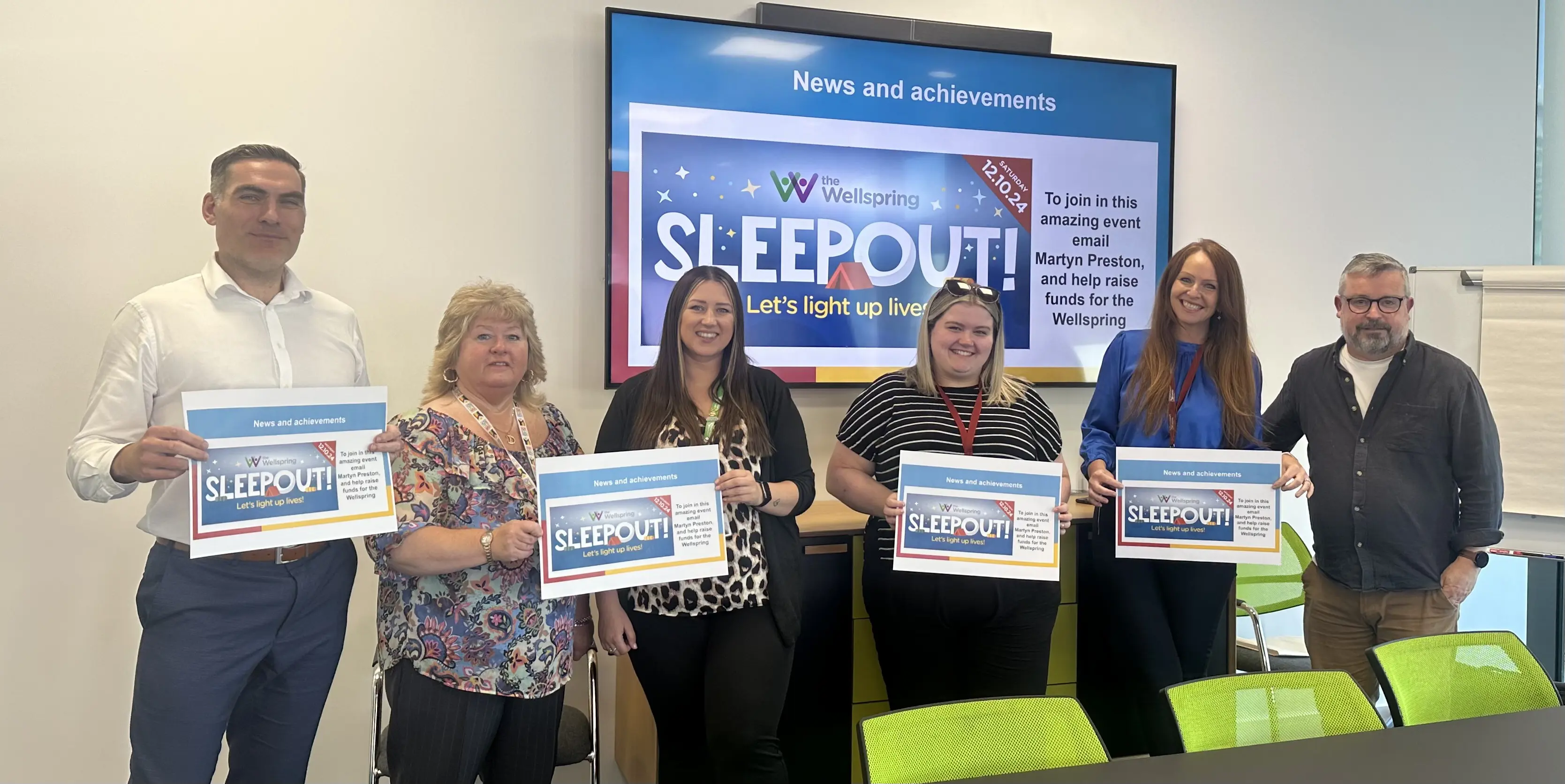 Collection of people in a board room with Wellspring sleepout signs