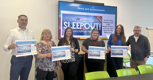 Collection of people in a board room with Wellspring sleepout signs
