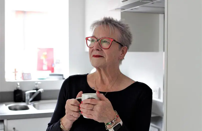 Woman inside a home wearing red glasses holding a mug