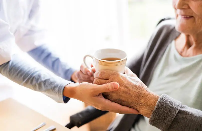 Older woman holding cup of tea in a mug with another woman's hands on their hands