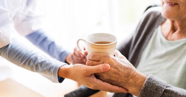 Older woman holding cup of tea in a mug with another woman's hands on their hands