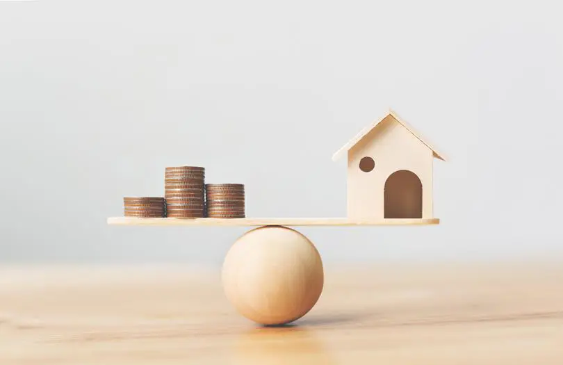 coins balanced on a ball against a wooden house