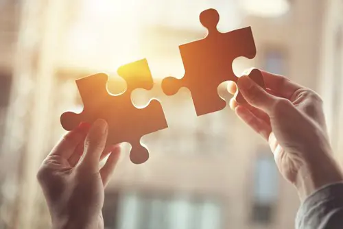 Two jigsaw pieces coming together in sunlight 