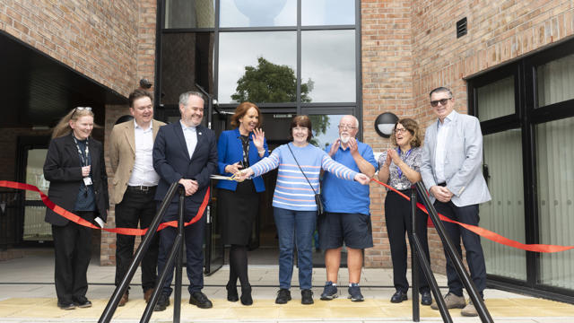Collection of people in front of building with a red ribbon being cut