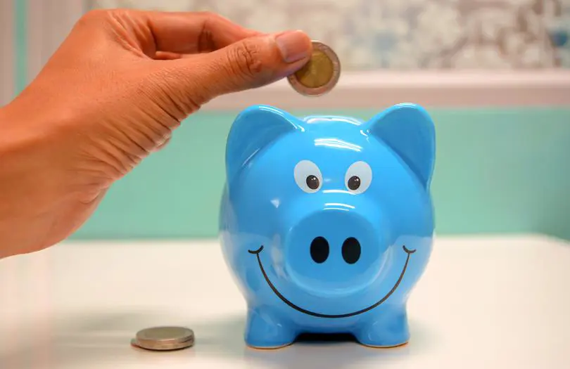 Blue piggy bank with hand placing coins into the top