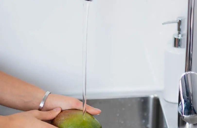hands washing a fruit over a sink